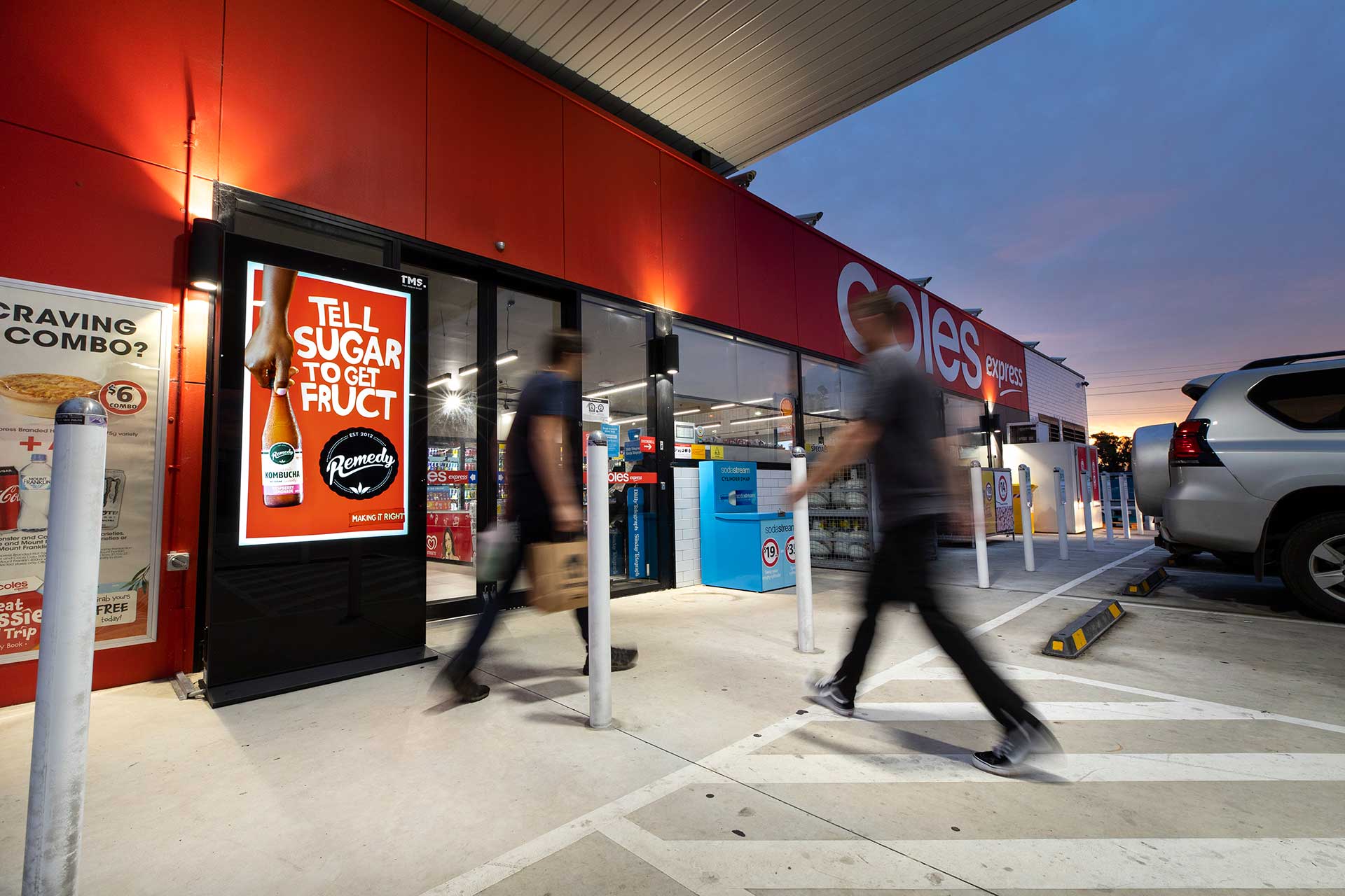 Digital advertising banner outside Coles Express service station entrance with people entering
