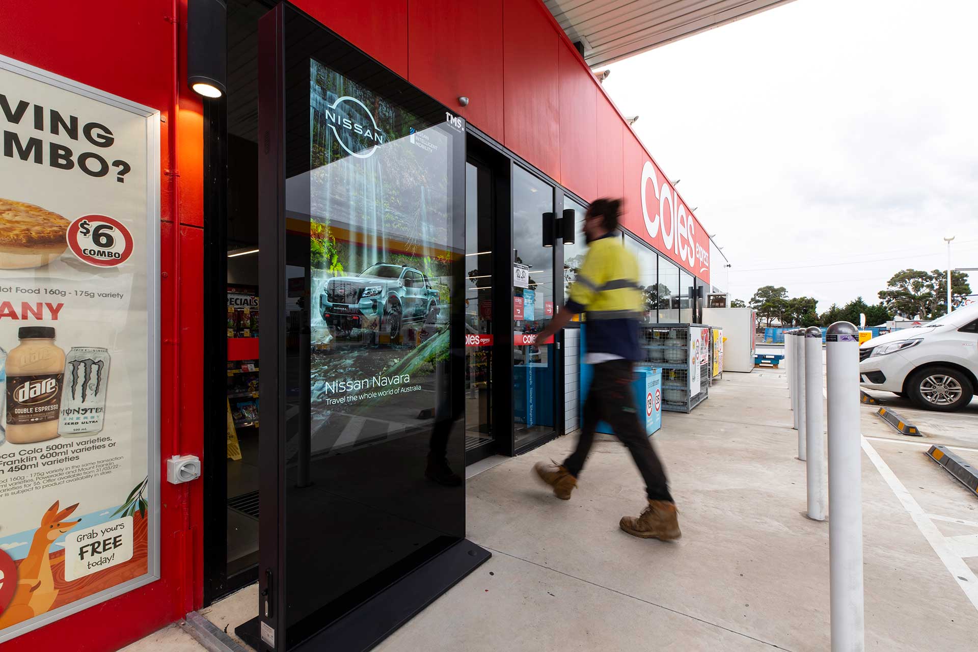 Digital advertising banner outside Coles Express service station entrance with man entering