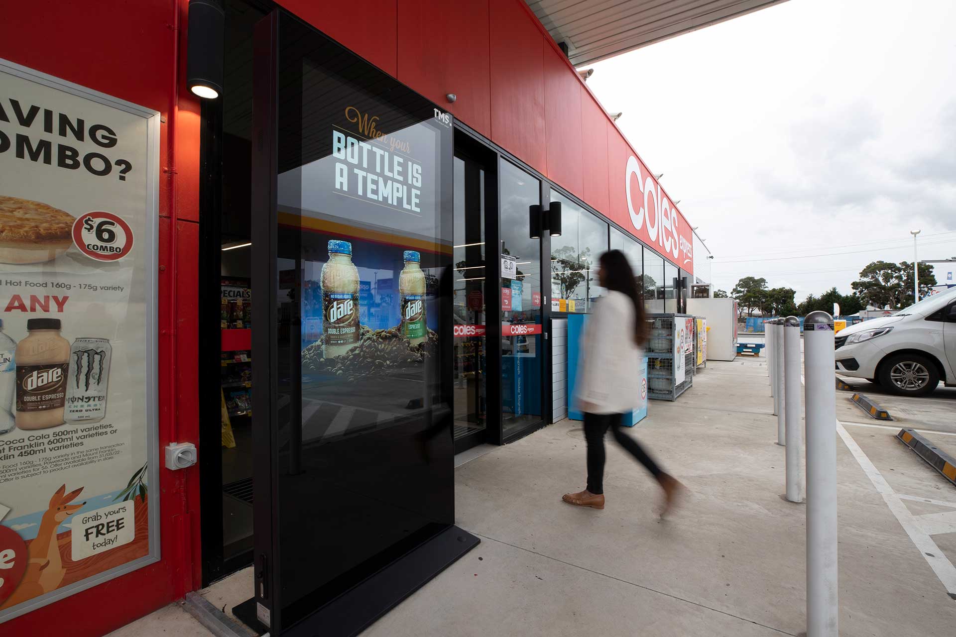 Digital advertising banner outside Coles Express service station entrance with woman entering