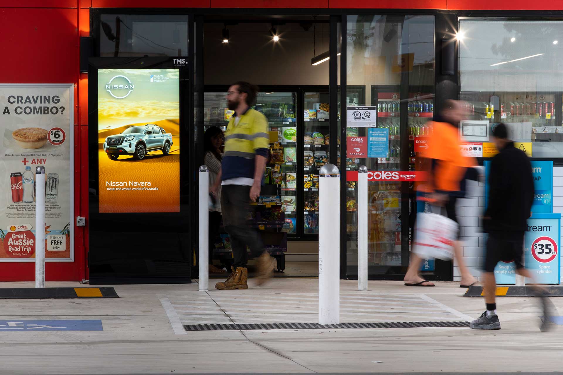 Digital advertising banner outside Coles Express service station entrance with man exiting